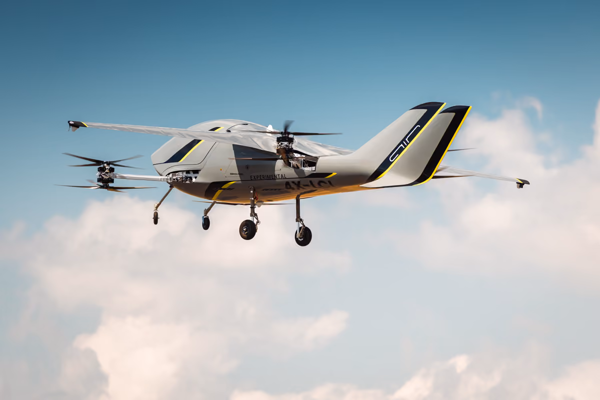 Experimental drone aircraft with four rotors flying in a clear blue sky with clouds.
