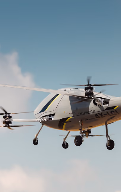 Gray drone helicopter flying in the sky with a clear background and landing wheels visible.