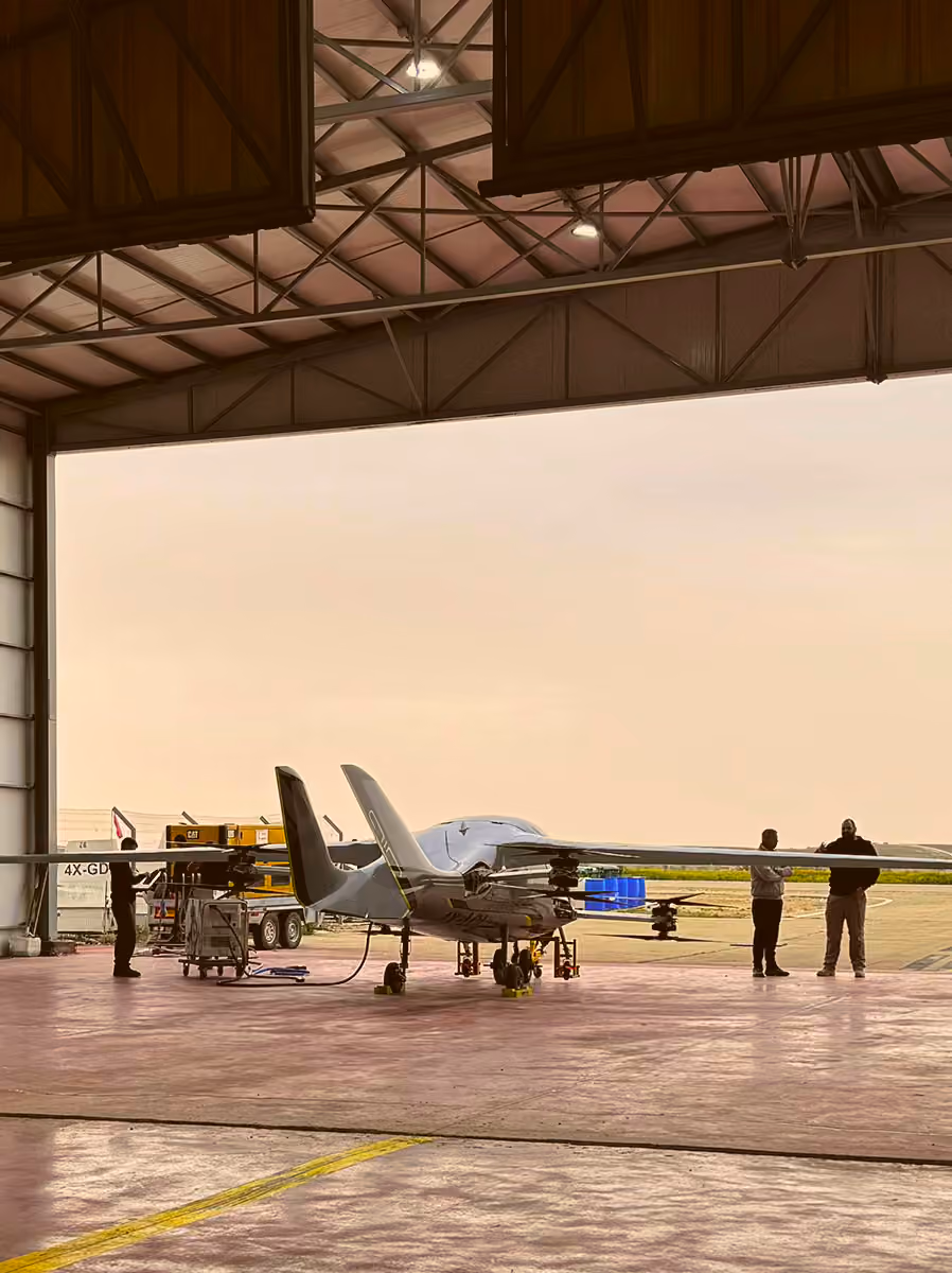 Small white aircraft inside a hangar with three people near the wings at sunset.