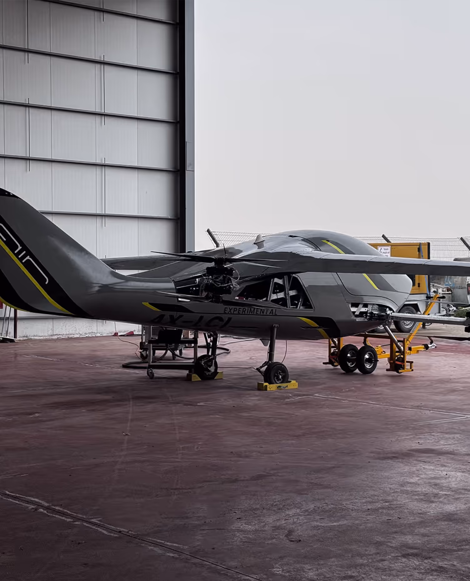 Gray experimental aircraft with yellow accents parked inside an aircraft hangar.