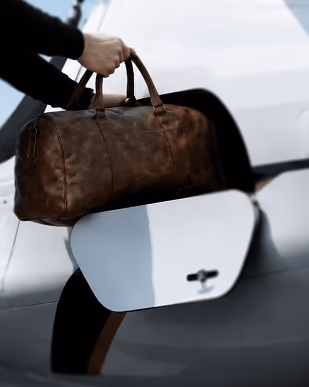 Person holding a brown leather bag while entering a white car through the door.