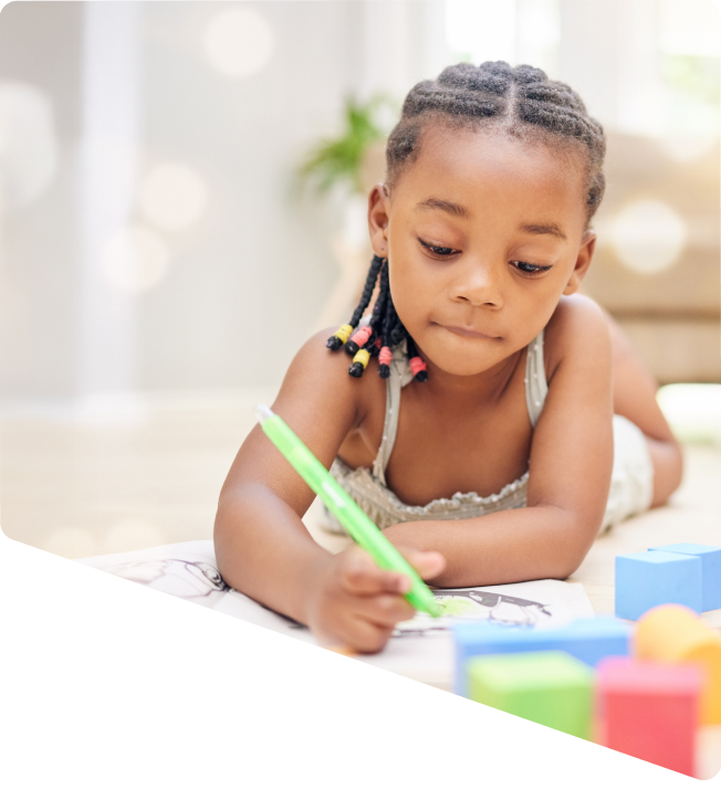 Young girl with braided hair coloring a picture with a green marker while lying on the floor.