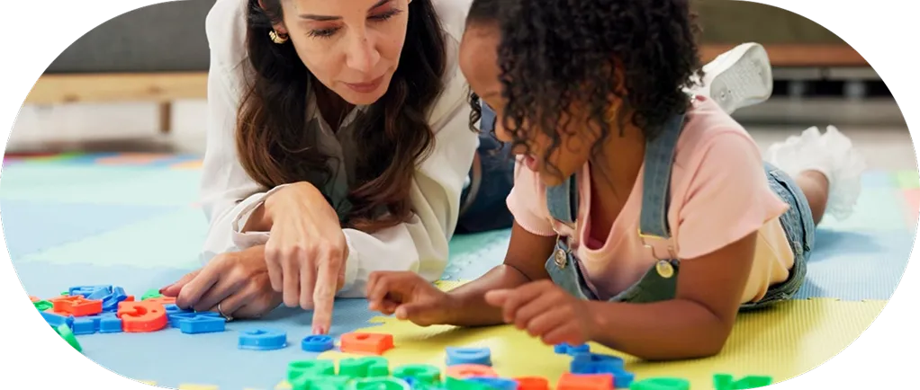Woman and child lying on a colorful mat playing with large, colorful alphabet letters.