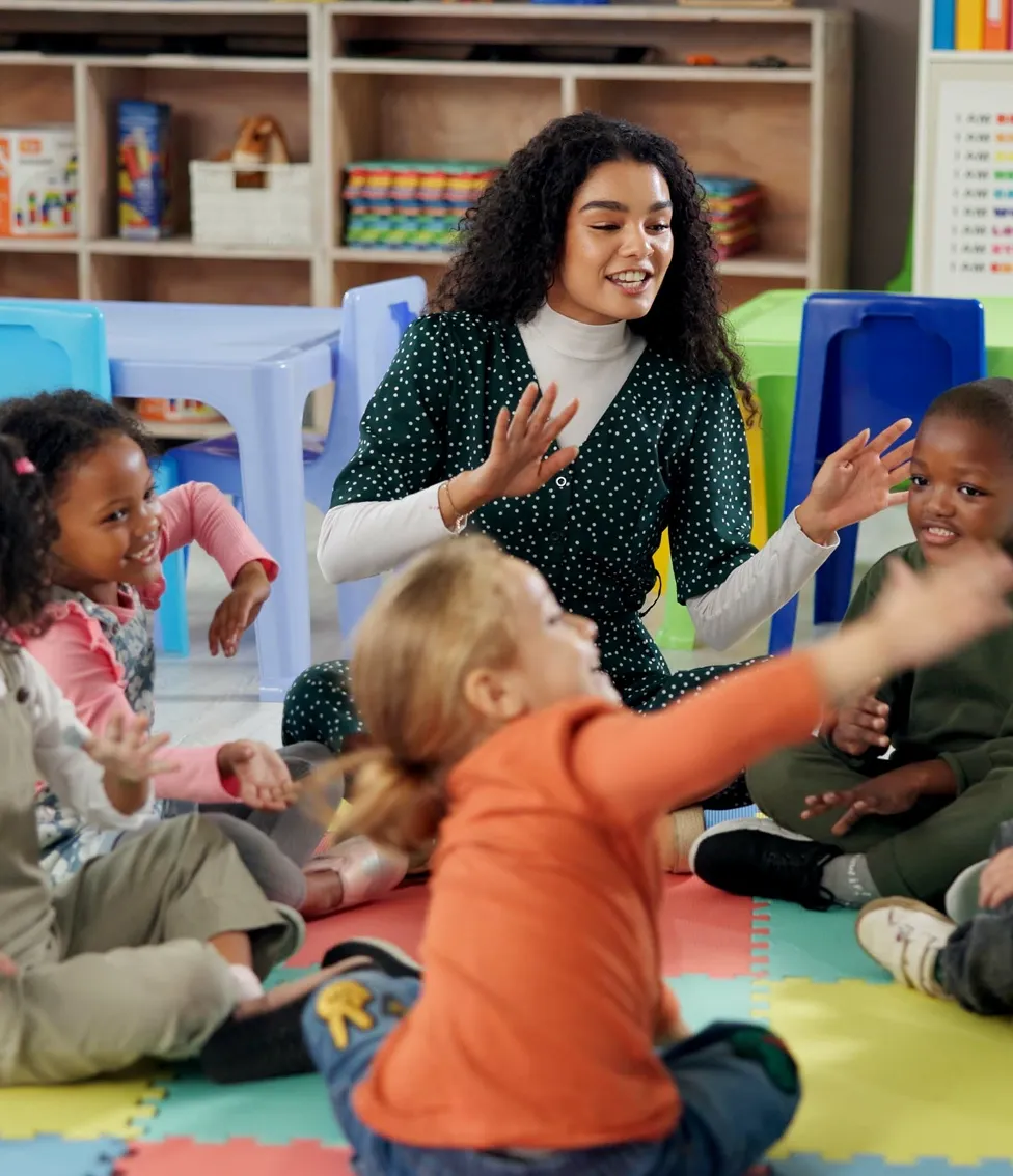 Teacher engaging with a group of young children sitting on colorful floor mats in a classroom.