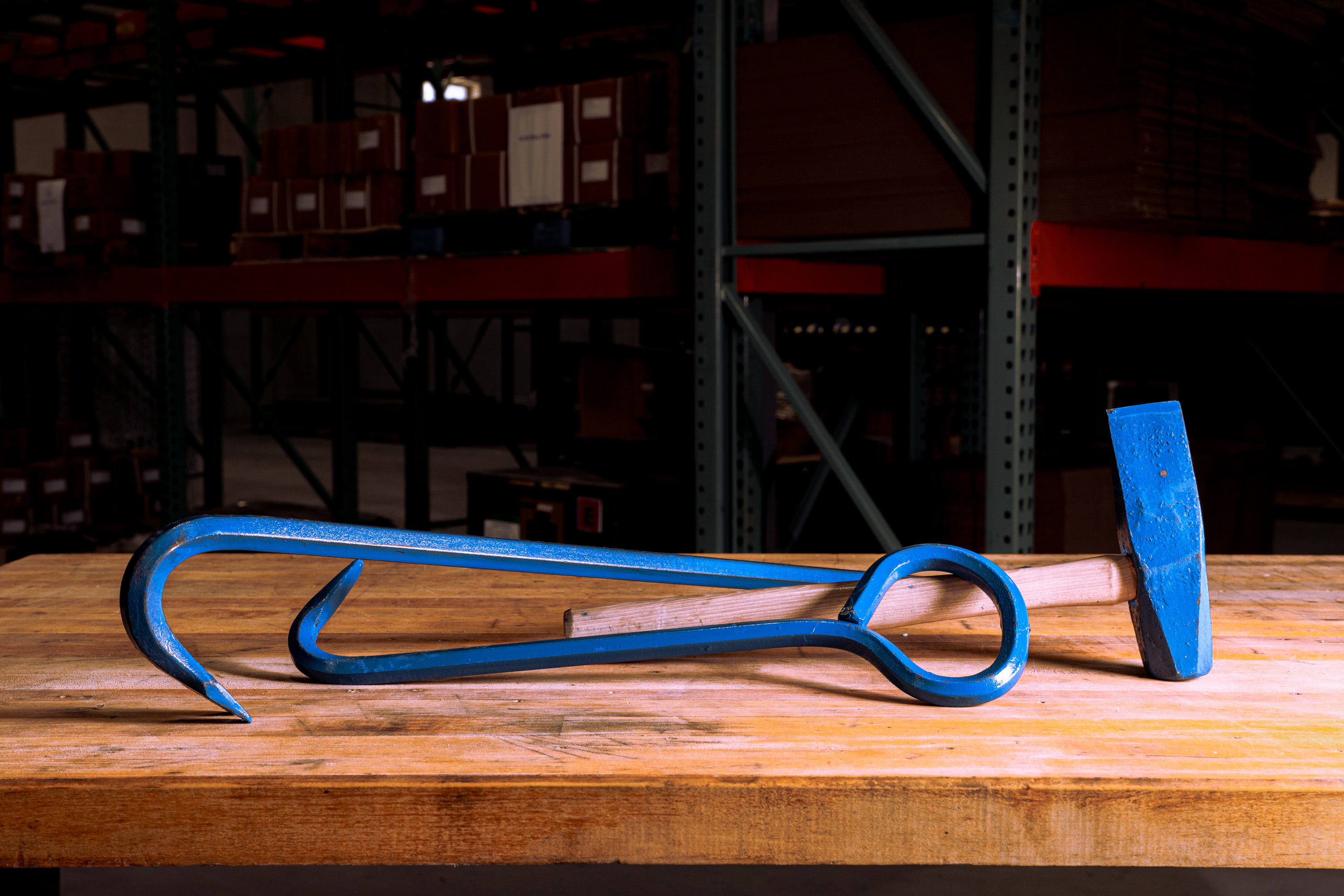 Blue-painted tire irons and a sledgehammer with a wooden handle on a wooden workbench in a warehouse.