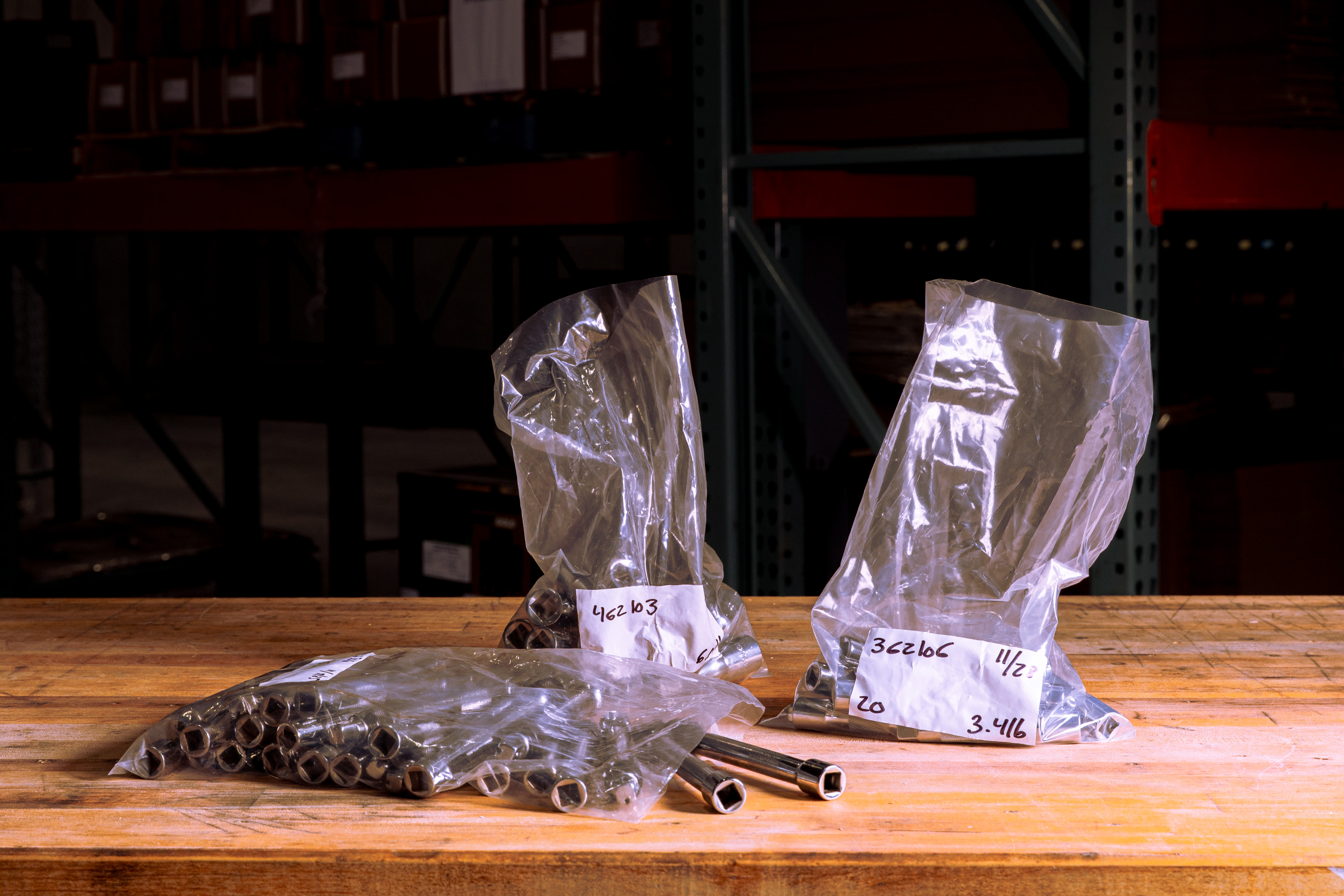 Three clear plastic bags filled with metal socket wrenches on a wooden workbench in a workshop.