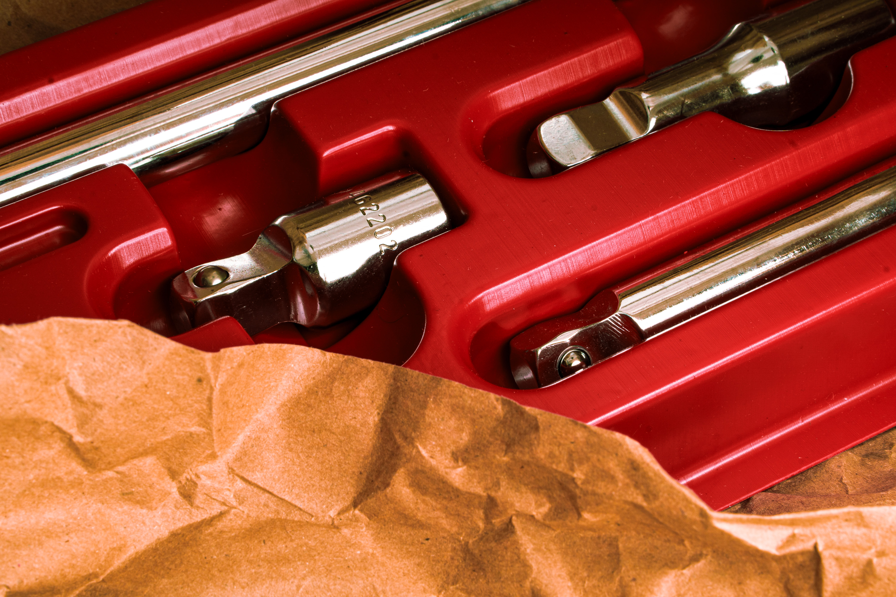 Close-up of metal tools in red plastic case partially covered by crumpled brown paper.