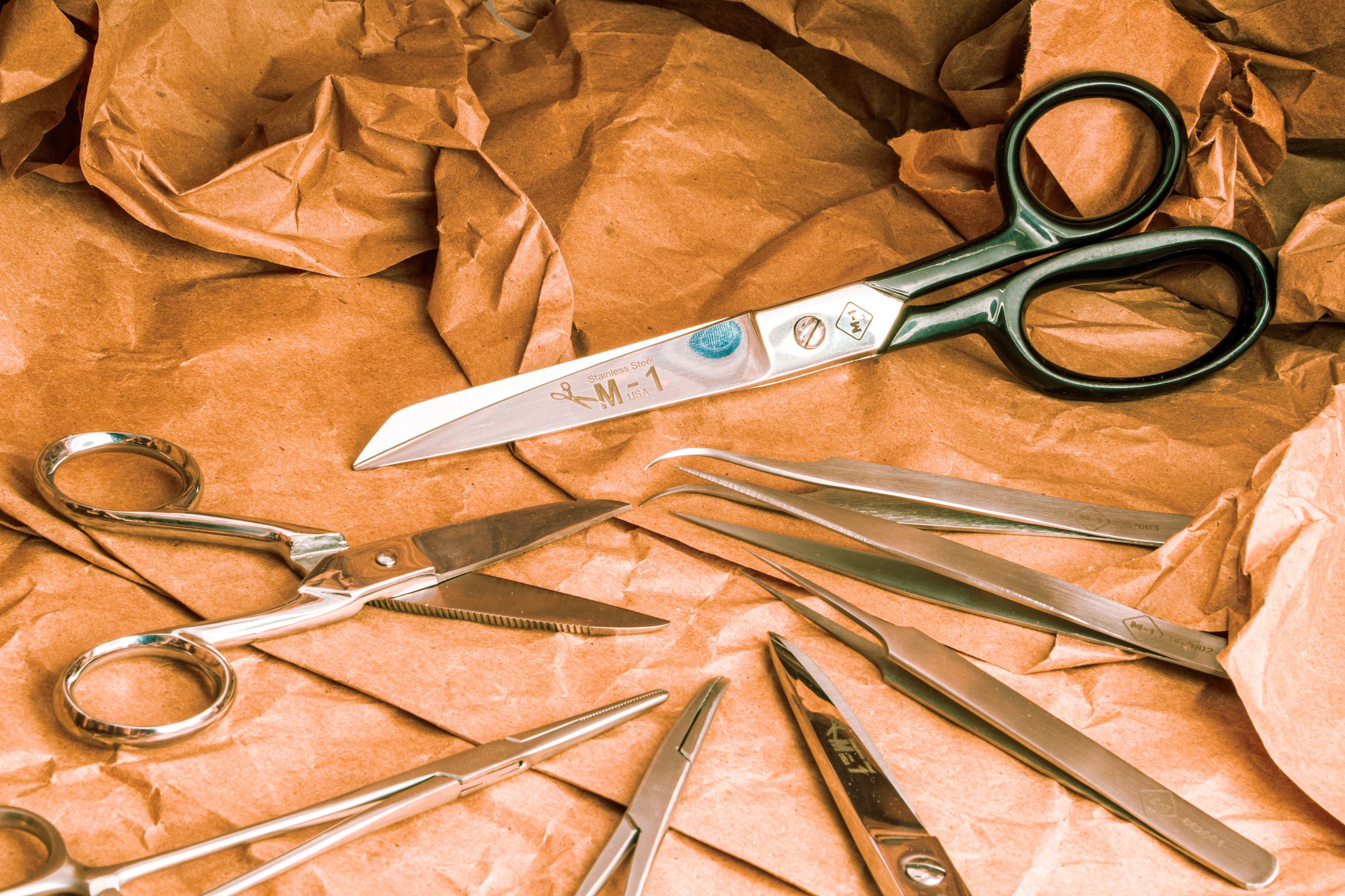 Various precision scissors and tweezers arranged on crumpled brown craft paper.