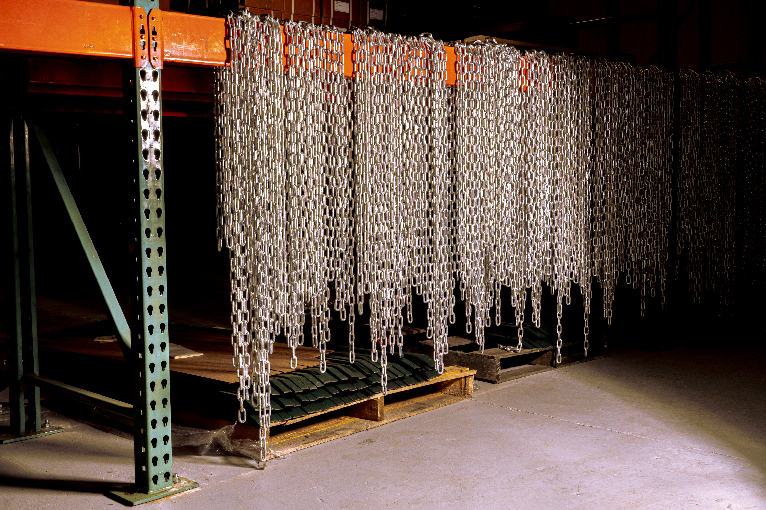 Metal chains hanging from an orange metal rack in a warehouse setting.