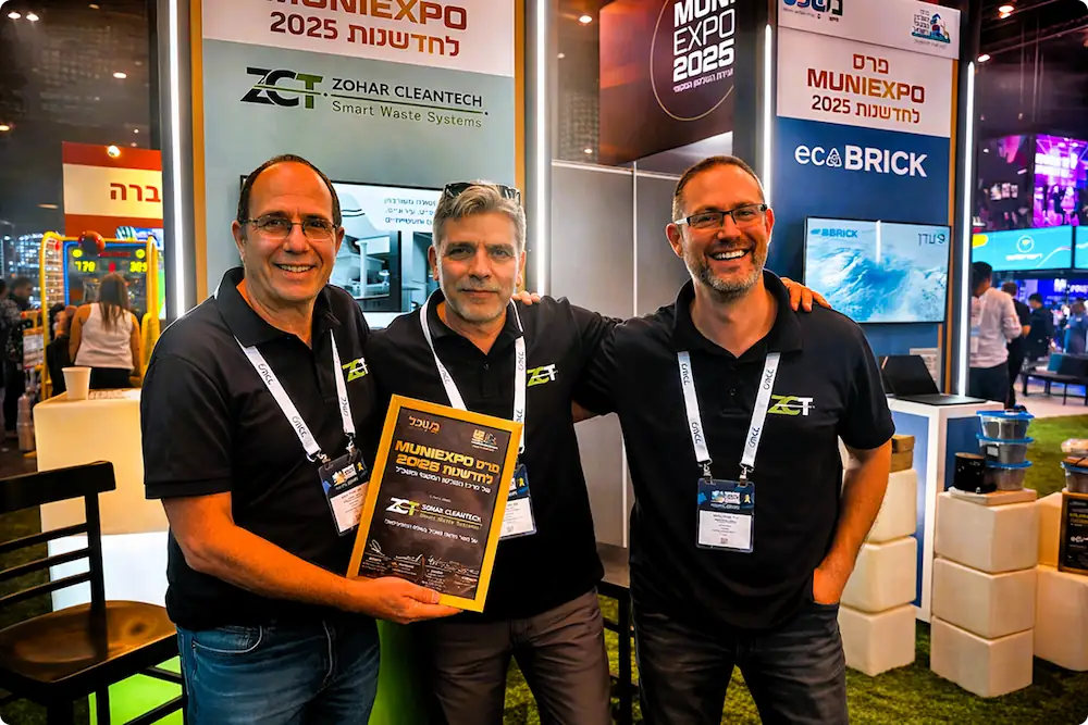 Three men wearing black ZCT shirts smiling, with one holding a framed MuniExpo 2025 award certificate at a trade show booth.
