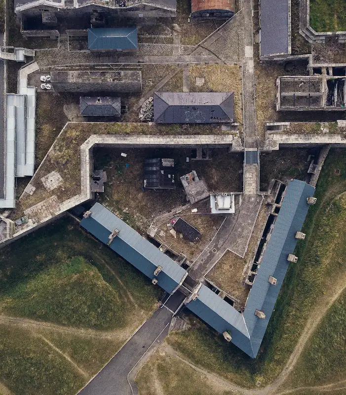 Aerial view of a historic stone fortification with angular walls, pathways, and several buildings within its perimeter surrounded by grassy areas.
