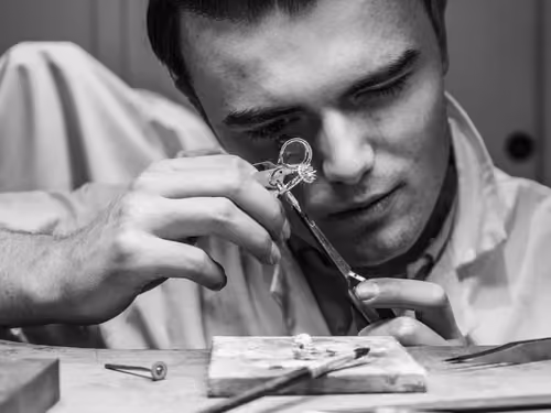 Un homme examine une bague avec une loupe de bijouterie en noir et blanc.