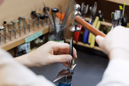 Un artisan bijoutier utilise un marteau pour travailler une bague fixée sur une enclume.