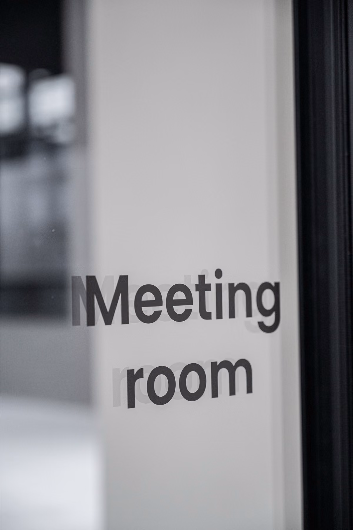 Glasdeur met tekst 'Meeting room' in een kantoorumgeving.