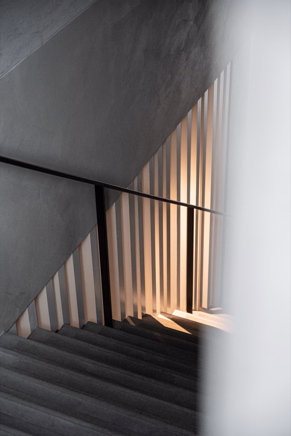Moderne trap met zwarte leuning en lichtdoorlatende witte tralies, verlicht door zacht warm licht.