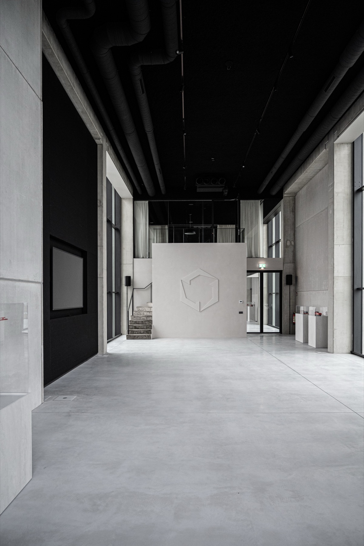 Ruim modern interieur met lichtgrijze vloer, witte muur met logo en zwarte plafondbuizen.