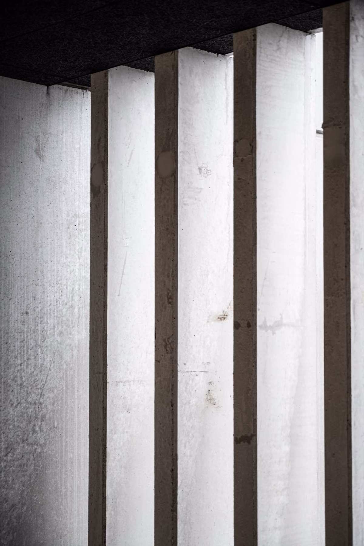 Vertical concrete pillars casting shadows on a light wall in an abstract pattern.
