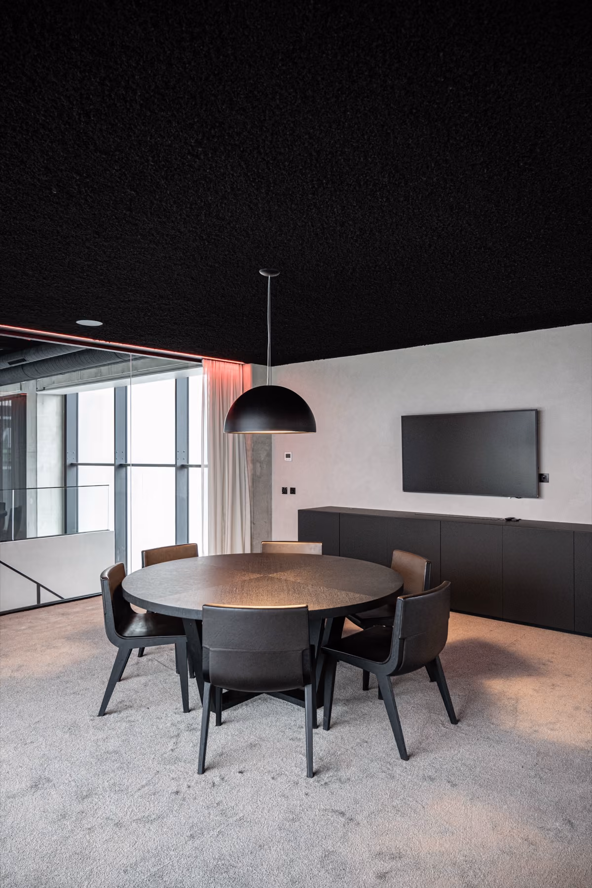 Moderne vergaderruimte met ronde tafel, zes zwarte stoelen en een beamer aan de muur.