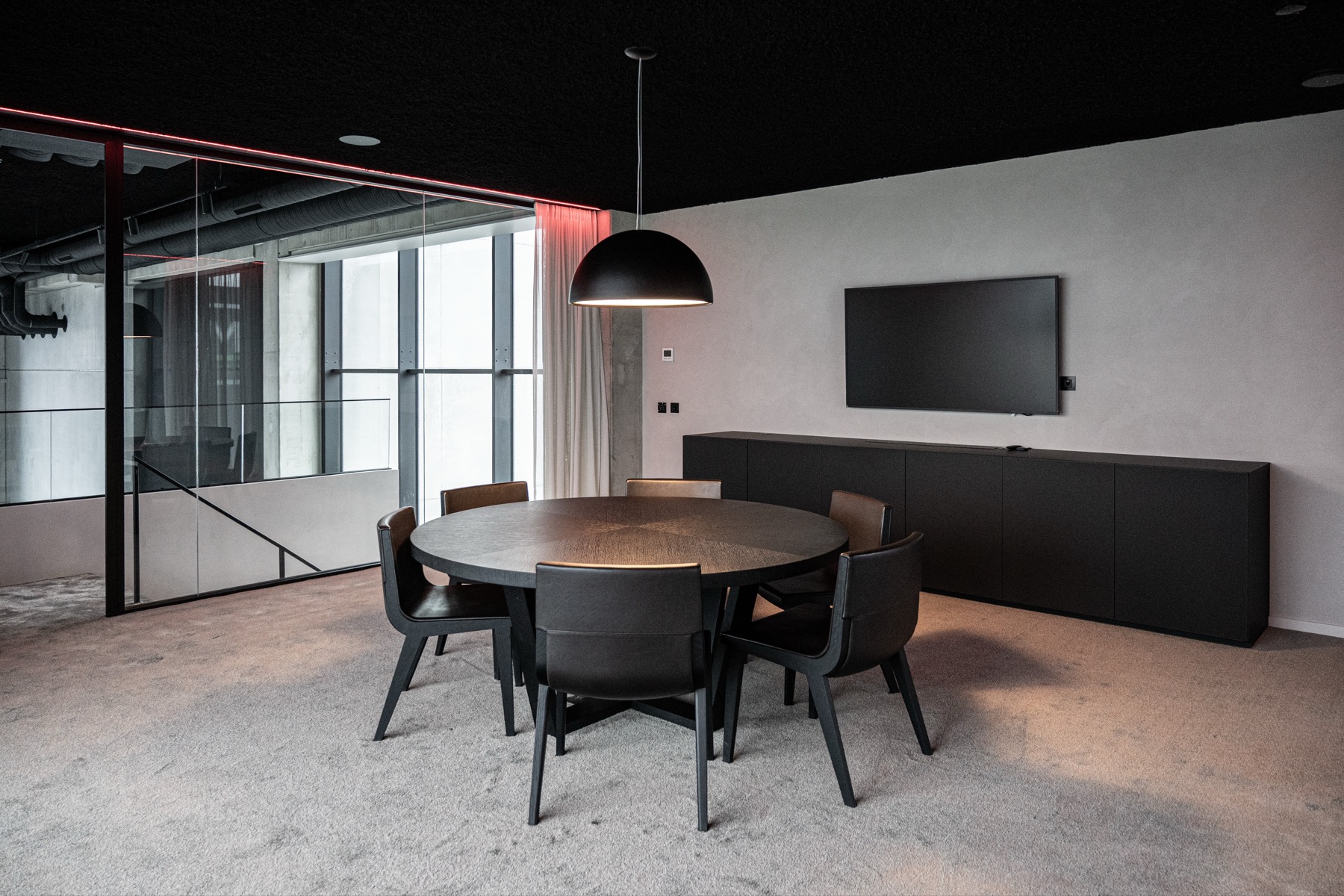 Moderne vergaderruimte met ronde tafel, zes zwarte stoelen, een hanglamp en een tv aan de muur.