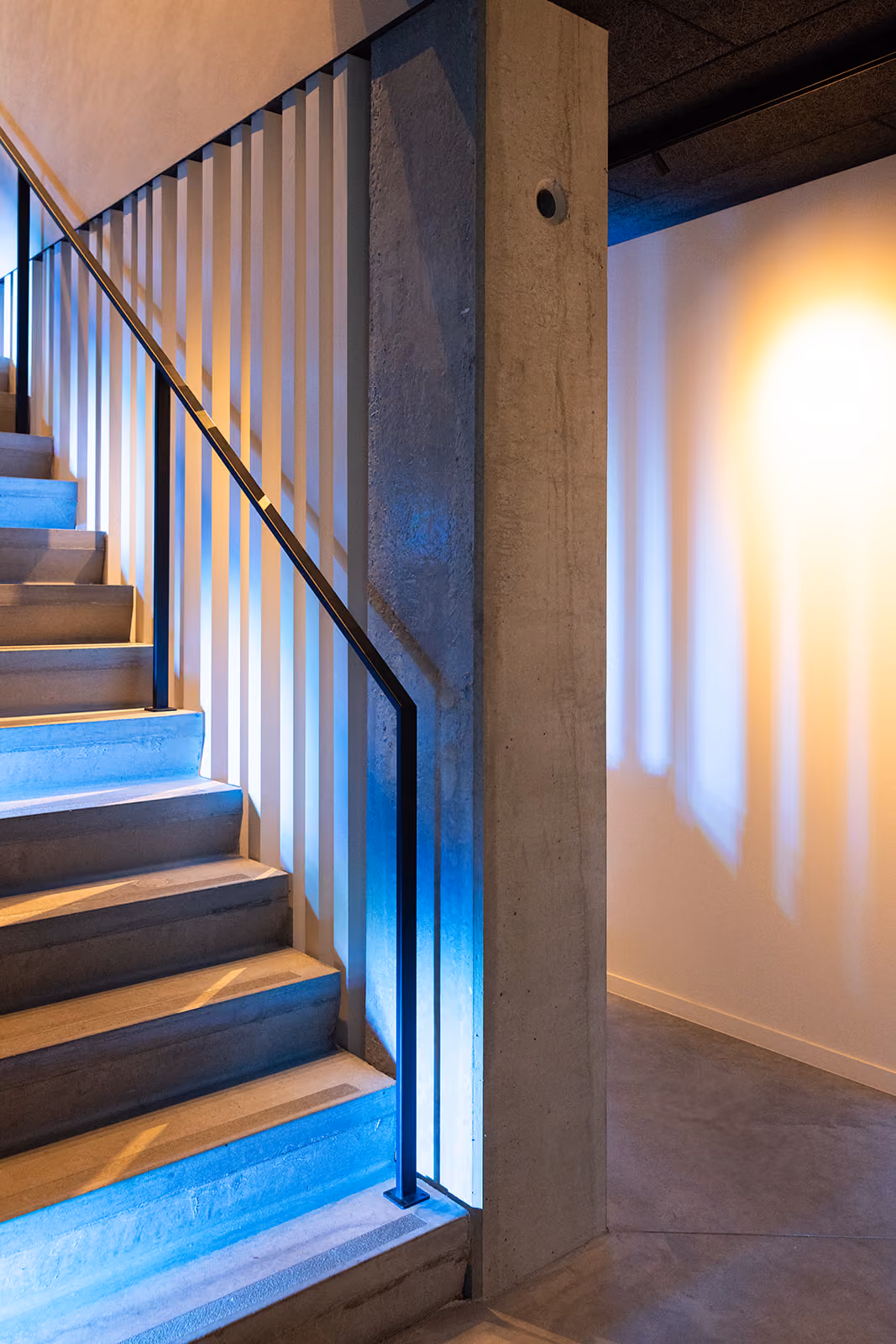 Moderne trap met betontrappen en metalen leuning verlicht door blauw en geel licht.