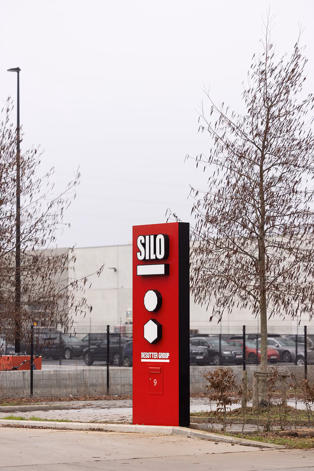 Rood SILO-bord met geometrische vormen en tekst DESUTTER GROUP, buiten bij parkeerterrein.