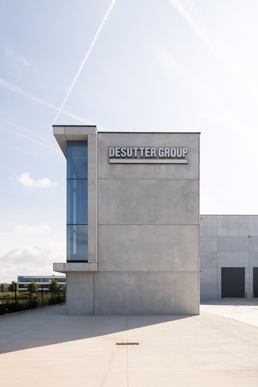 Modern concrete building with large glass window and DESUTTER GROUP sign on clear sky background.