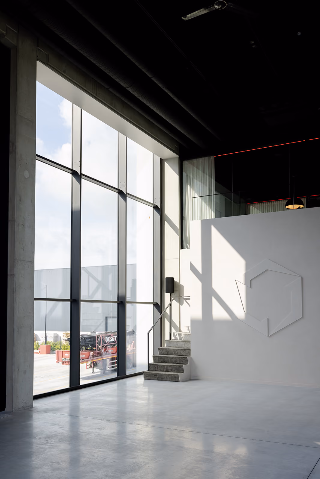 Lichte industriële hal met grote ramen, trap en abstracte wanddecoratie in wit interieur.