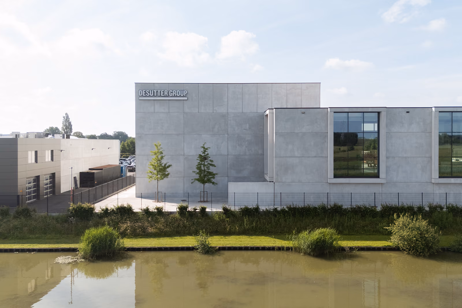 Modern concrete building with large windows and Desutter Group sign beside a water canal.