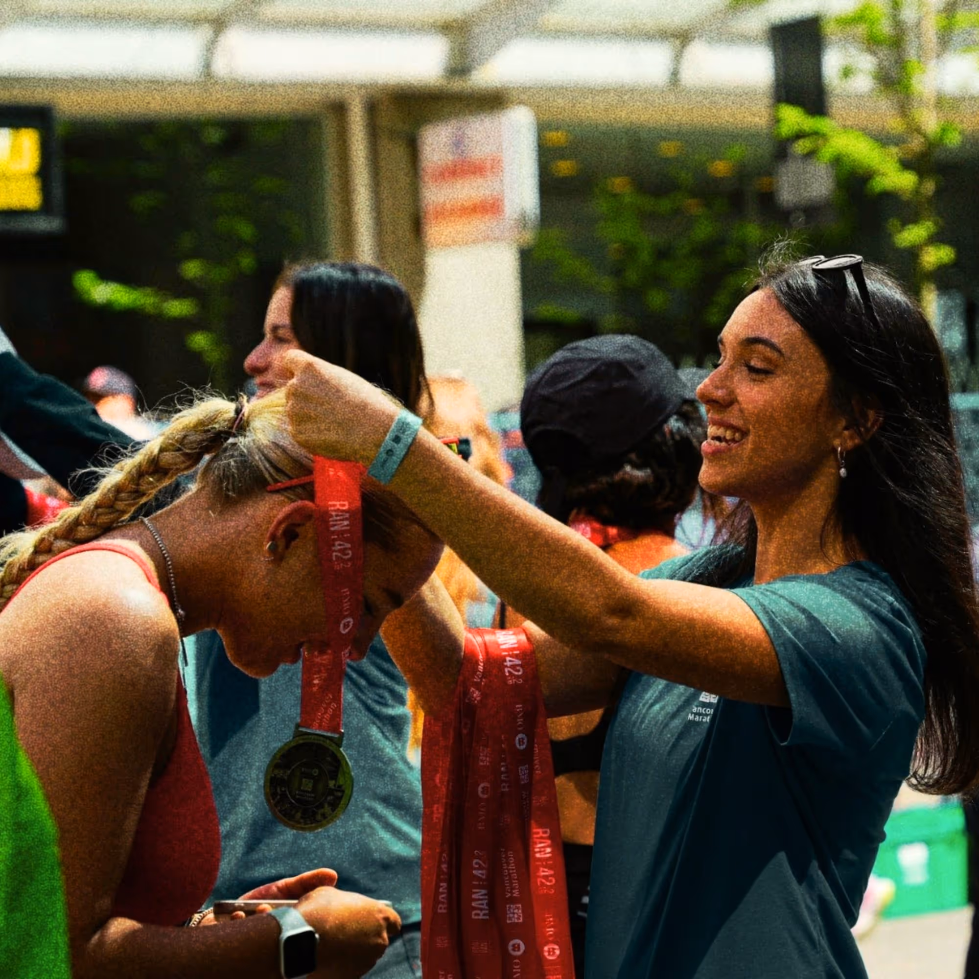 Woman smiling as she places a marathon finisher medal around another woman's neck with braided hair.