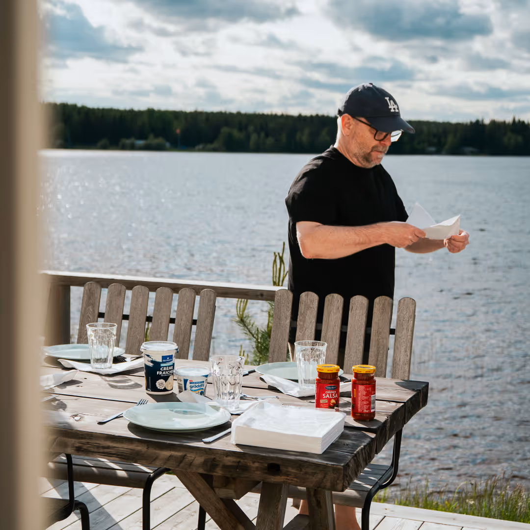 Person står vid ett matbord utomhus med vatten i bakgrunden