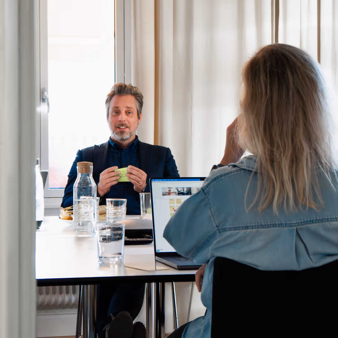 Två personer står och pratar med kaffekoppar i handen i en verkstadsmiljö – en avslappnad och genuin stund under arbetet.