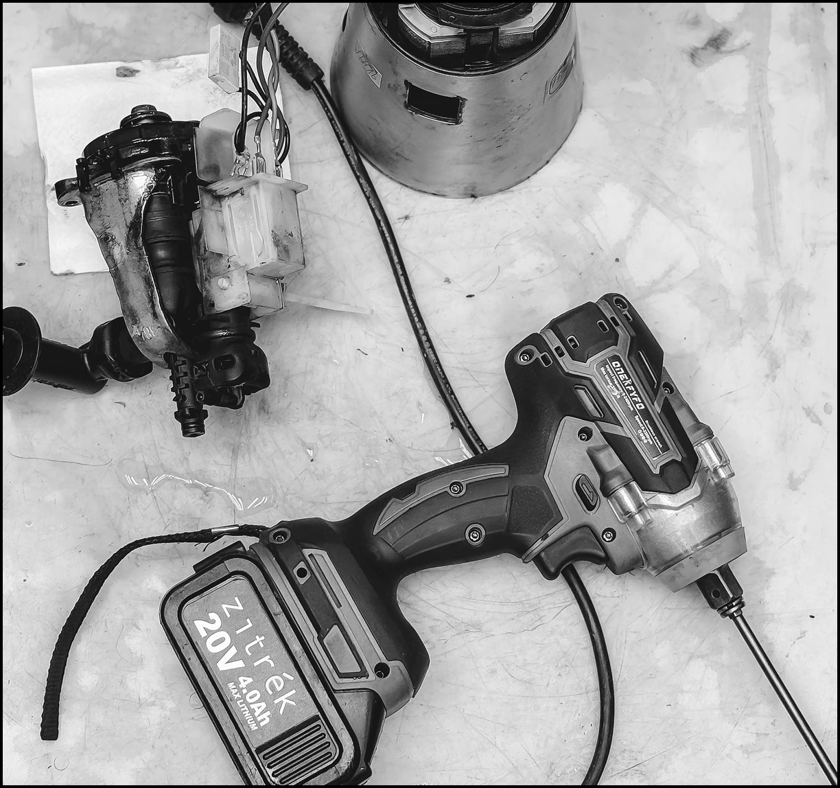 Cordless power drill with a 20V 4.0Ah battery and a screwdriver bit attached, placed on a workbench with other mechanical parts.