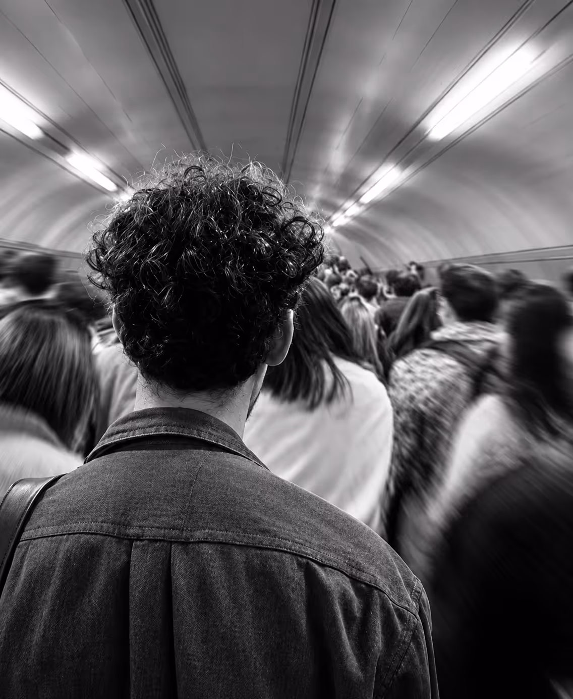 A tunnel filled with people all walking down in one direction, centred behind one person with curly hair.