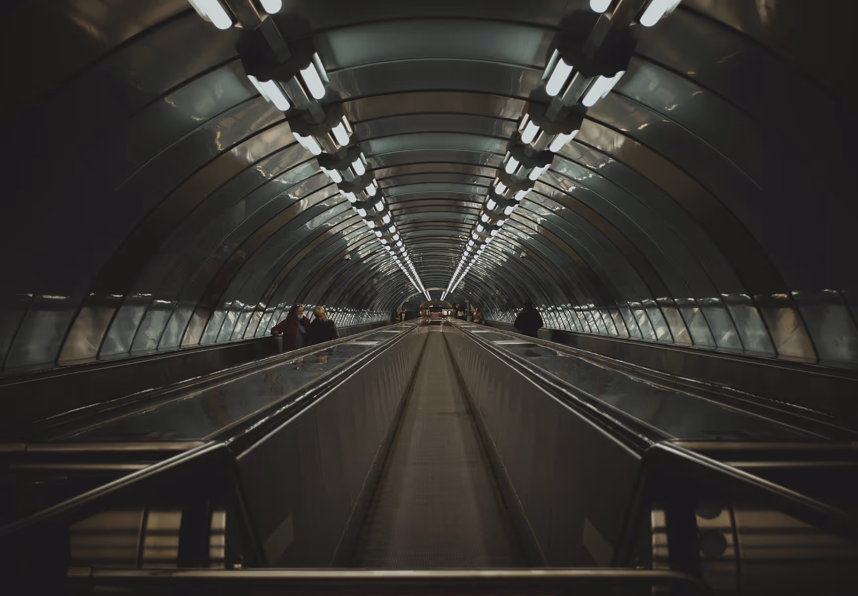 Long underground tunnel with two parallel moving walkways and few people walking alongside them.