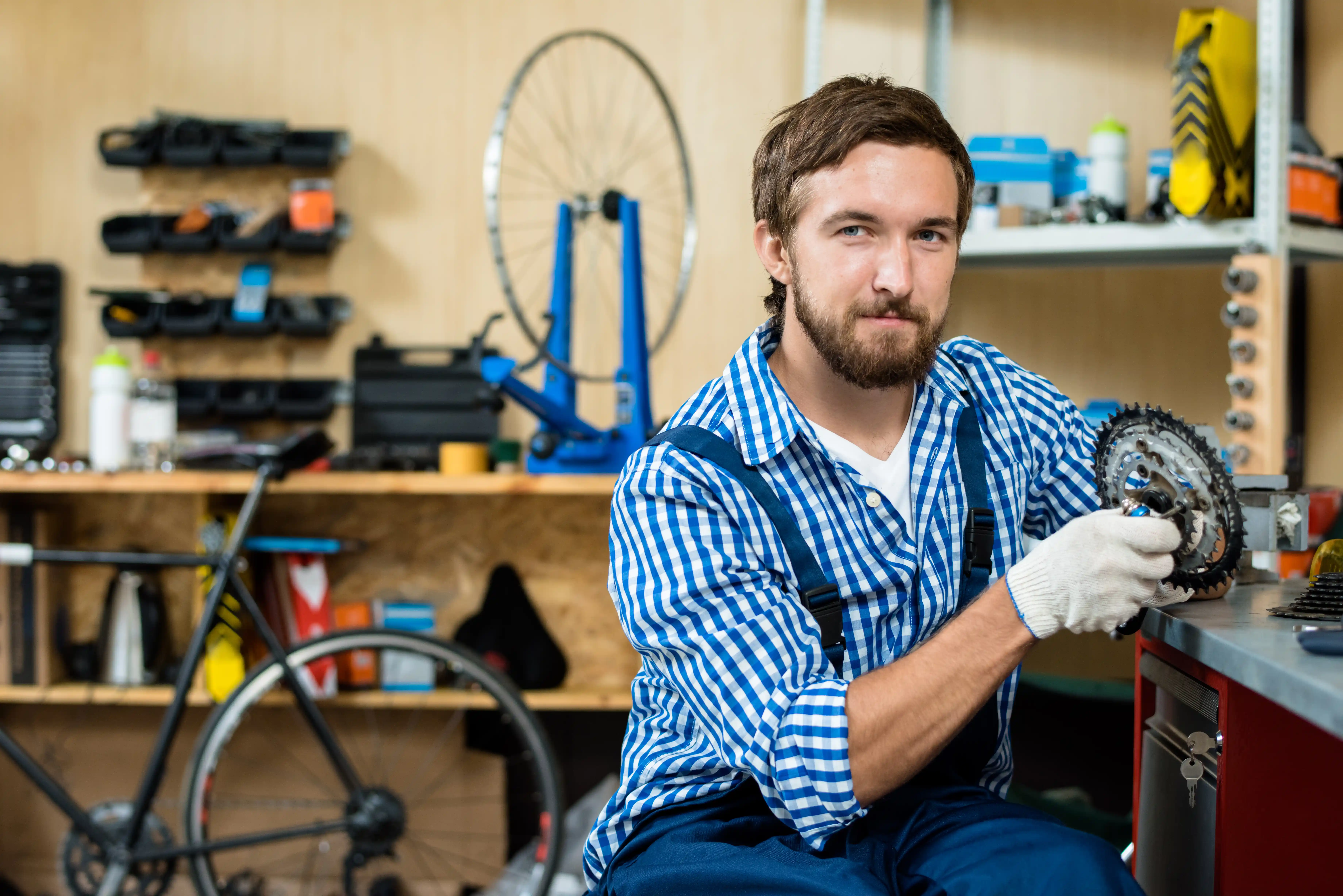 Mechanic in a blue overall works on a tablet under a car in a garage. The setting is organized, with cars and tools visible, conveying focus and professionalism.