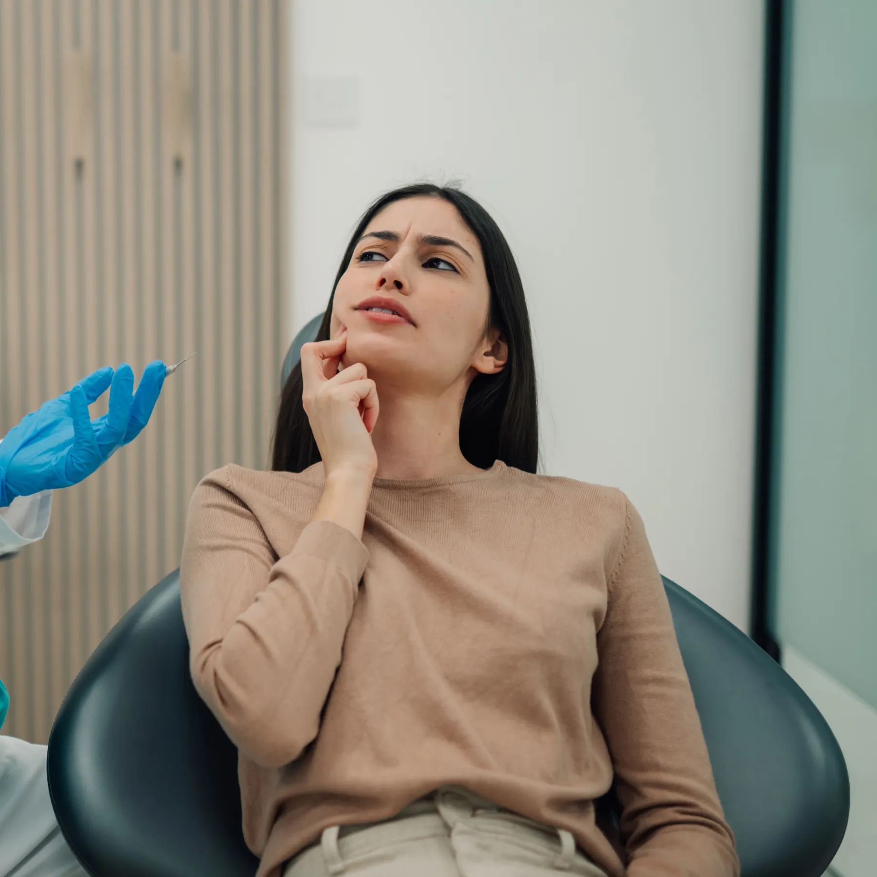 Woman with tooth pain sitting in a dental chair as a gloved hand holds a syringe.