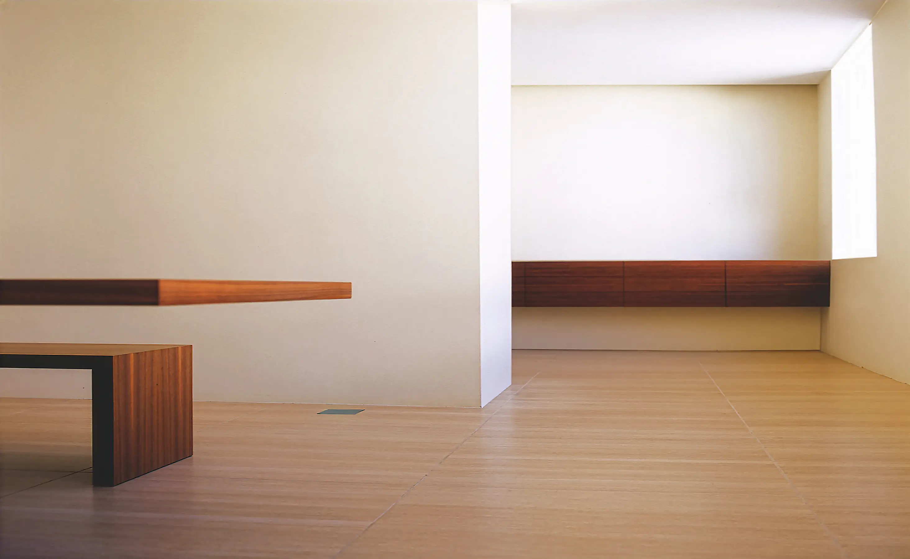 The kitchen comprises a band of black oak and steel, a worktop with drawers cantilevered off the wall, seamless induction and a black sink. The wall conceals the full-height units and pantry beyond. Lighting washes down from full-length ceiling slots.