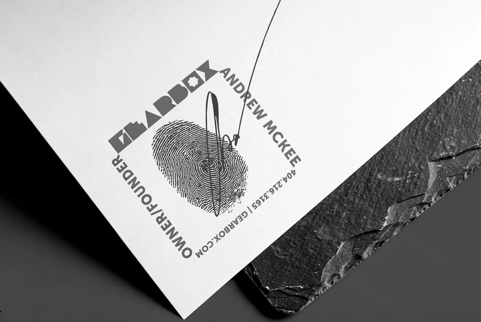 Gearbox letterhead on slate with the wordmark, contact line and a fingerprint mark pierced by a scribe