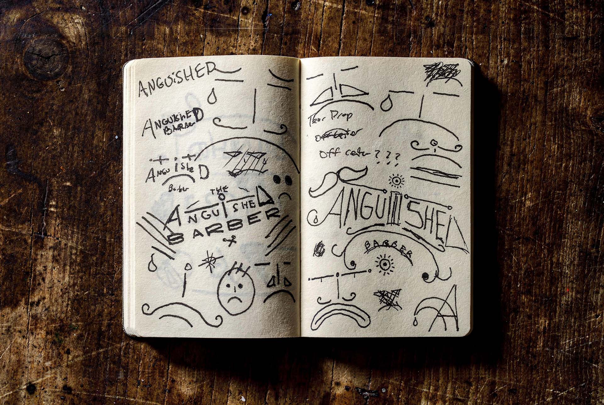 An open field notebook on a wood table, both pages filled with quick marker sketches working out the Anguished Barber logotype