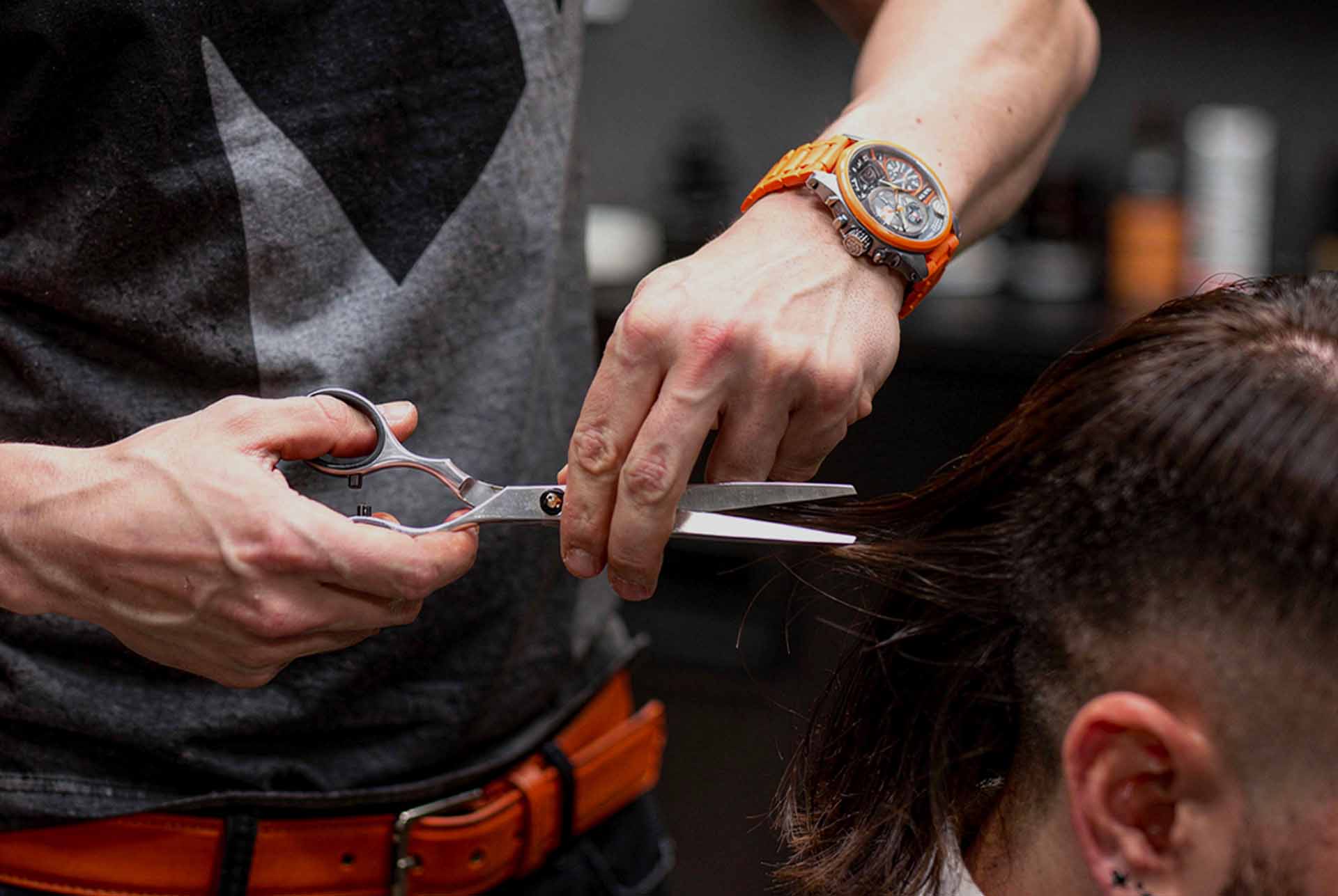 A barber in a dark apron cutting a client's hair with shears and comb in the shop