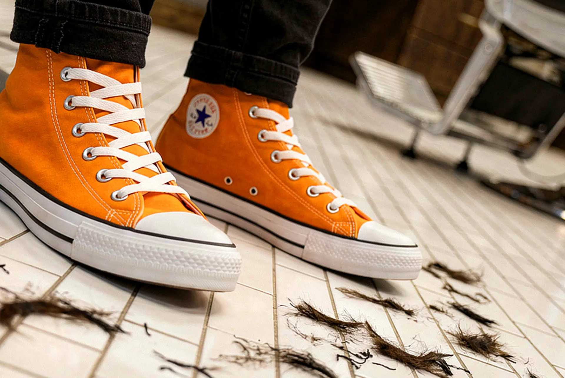 Orange De León uniform high tops on a white tiled barbershop floor covered in cut hair