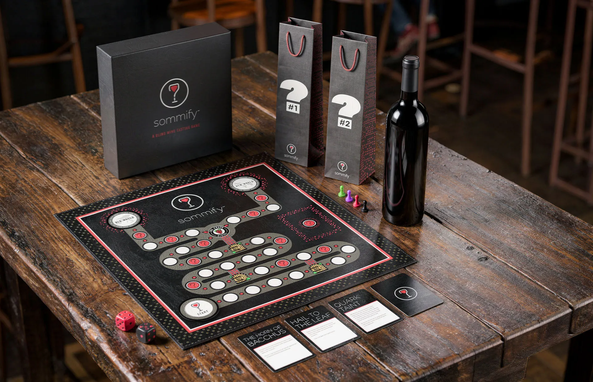 The finished Sommify game set out on a wood table, the board with pawns and dice, the boxed set behind it, two numbered wine bags, a bottle and score cards