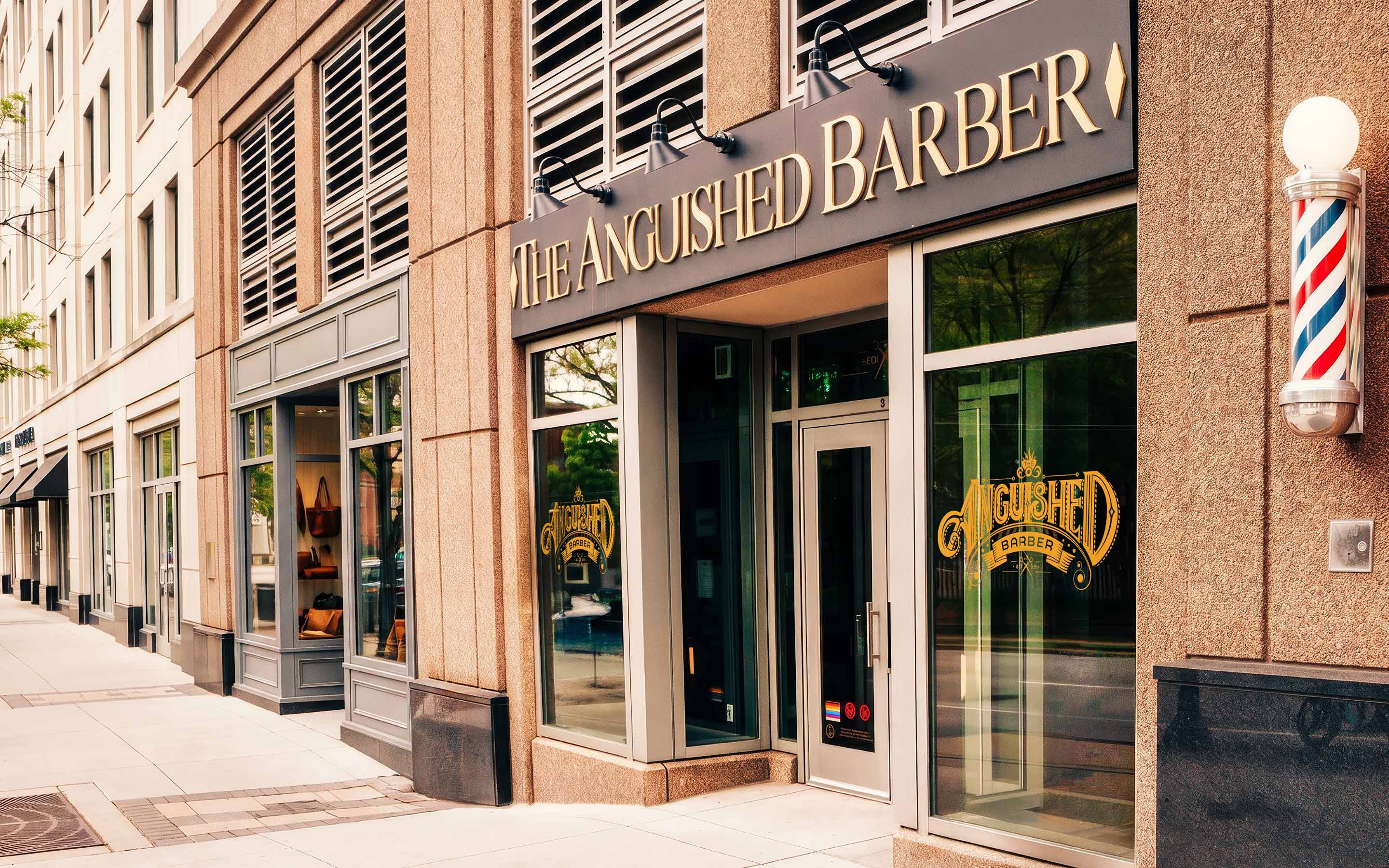 The Anguished Barber storefront with gold window lettering and a barber pole