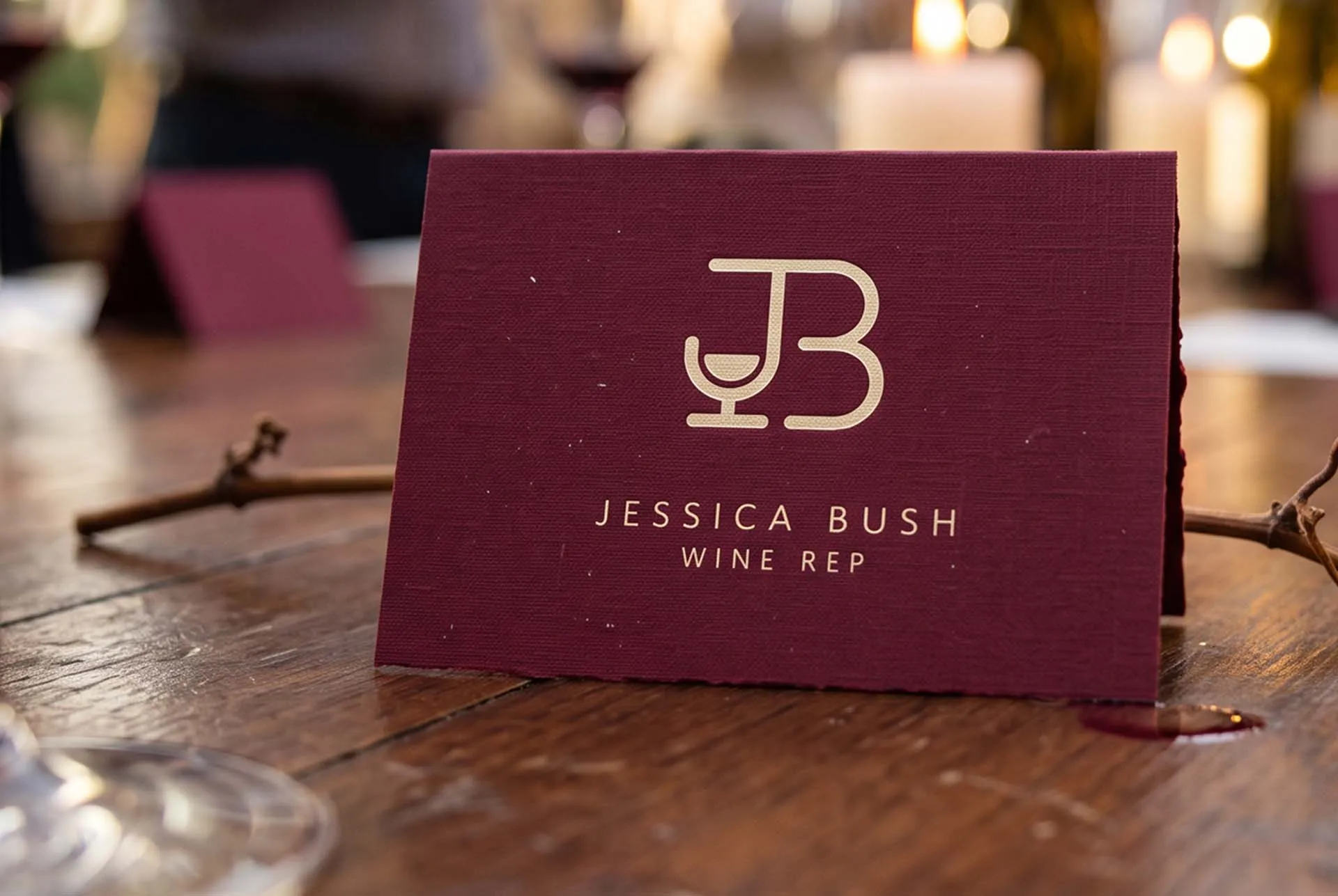 A burgundy Jessica Bush business card standing on a table beside a pair of glasses