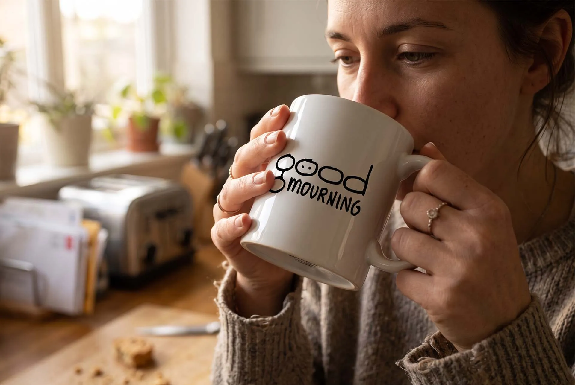 A woman drinking from a Good Mourning mug in a kitchen