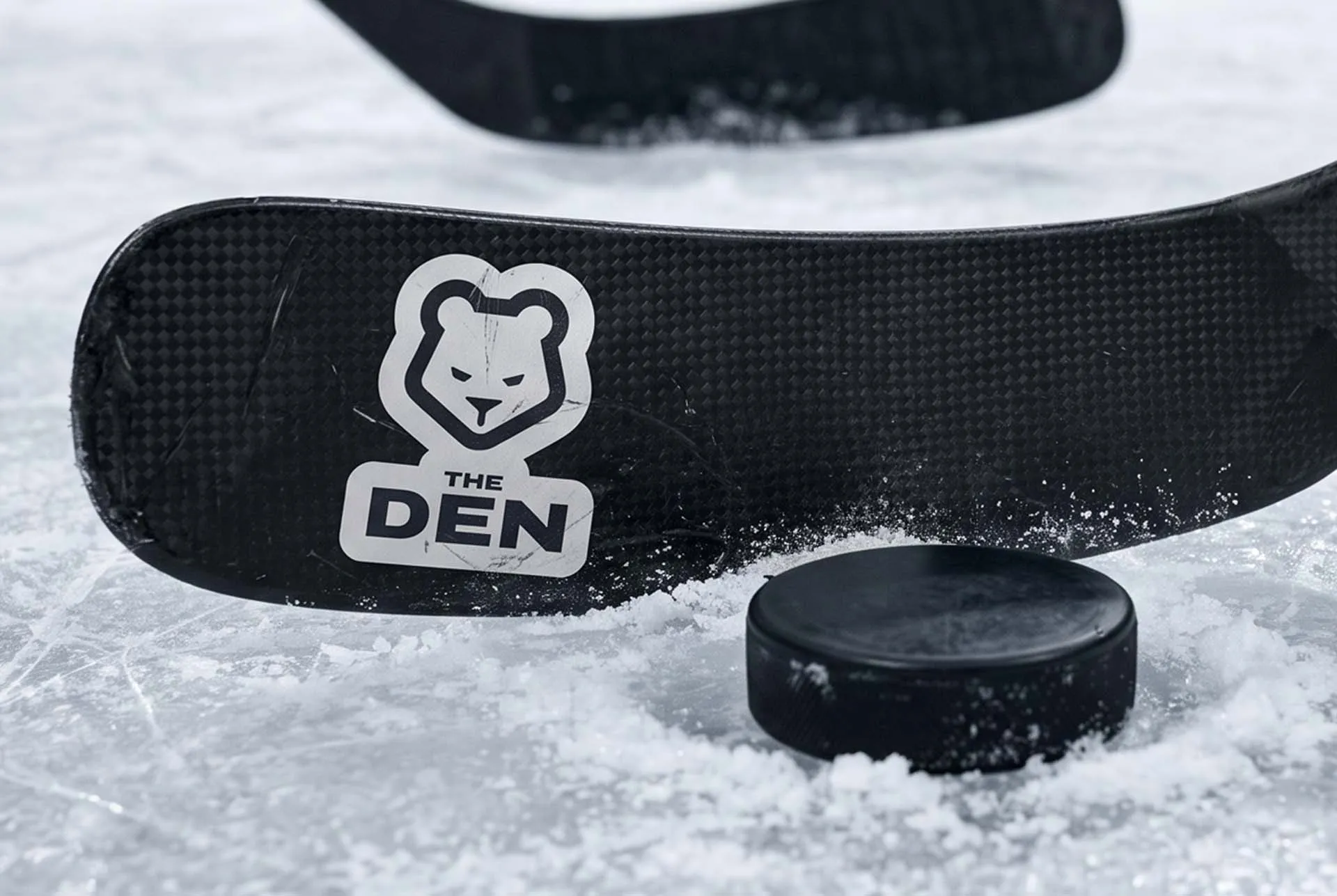 The Den mark printed on a hockey puck resting on ice