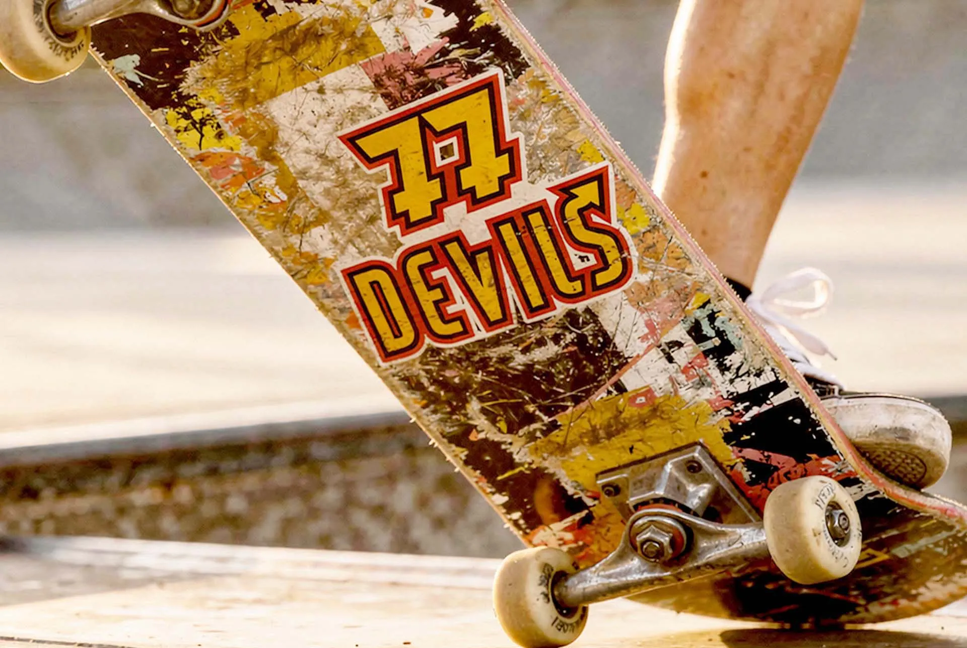 A skateboard deck printed with the 77 Devils mark, held up on a ramp