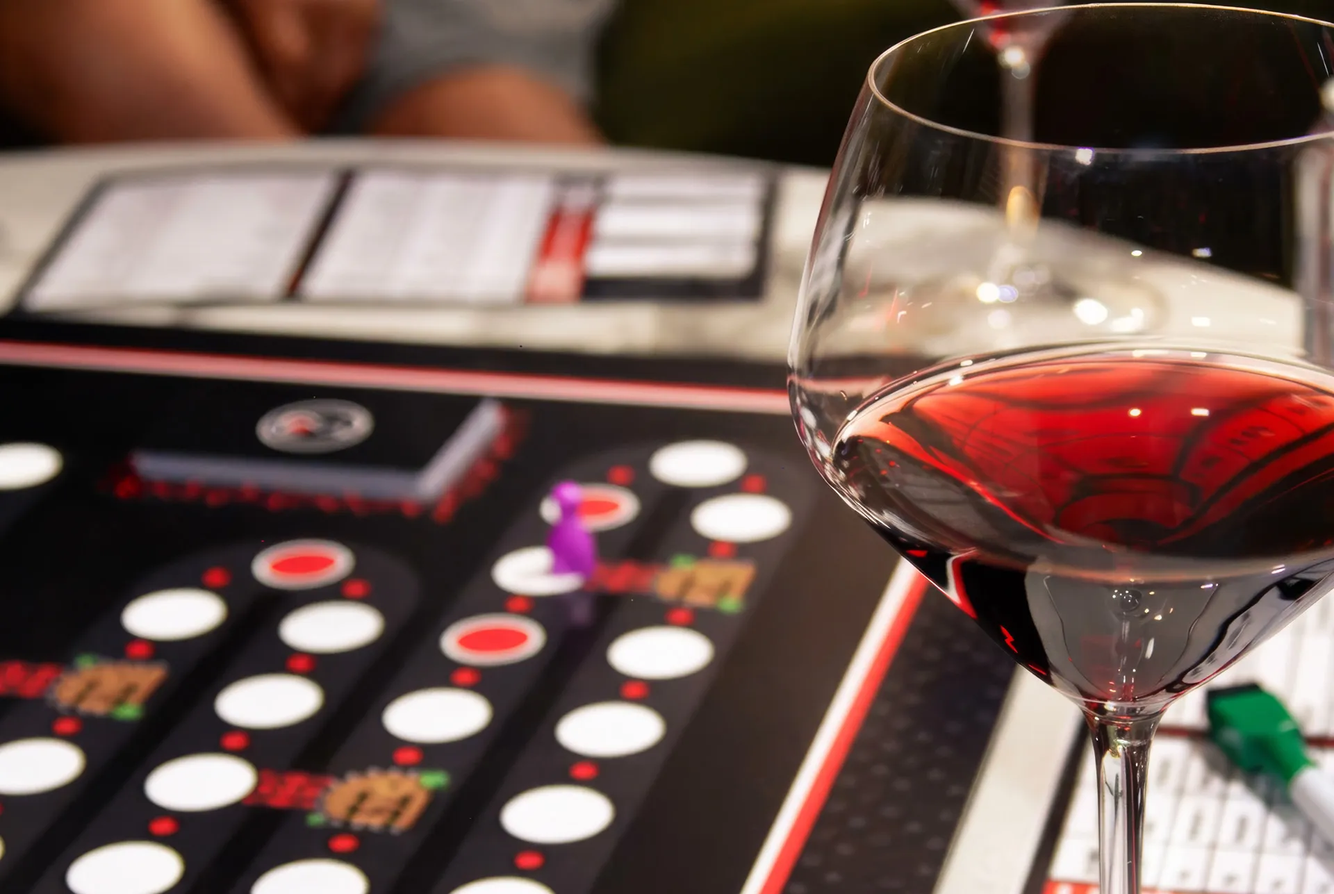A glass of red wine standing beside the printed Sommify board with its pawns in play