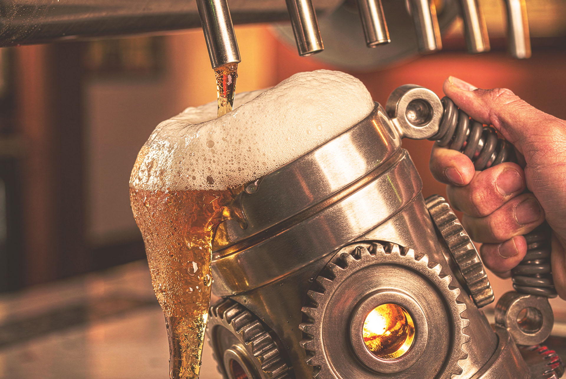 Beer pouring from a tap into a Gearbox stein built from a gear housing with a coil spring handle, held at a bar