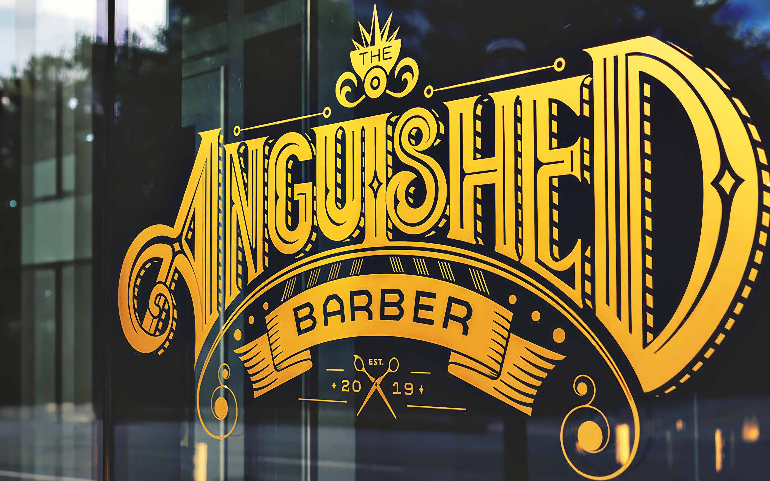 The Anguished Barber gold logo lettering on the shop's storefront glass